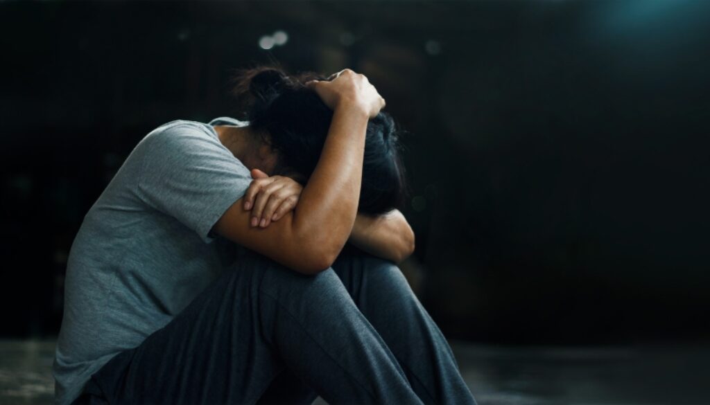 Woman sitting on the floor in a dark room in a hunched position.
